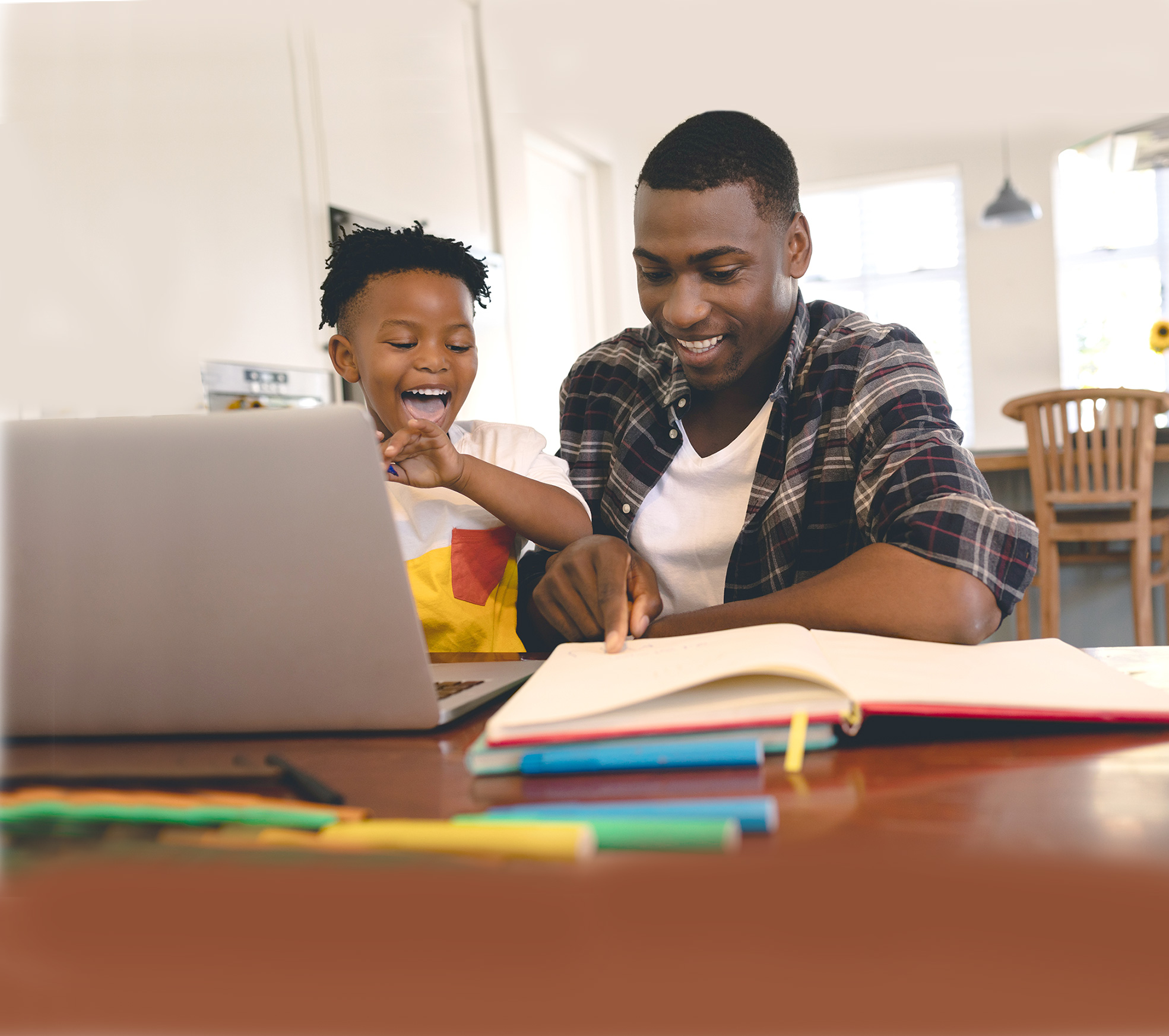 Man of colour and his son on computer at kitchen table smiling